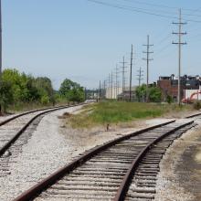 Diverging tracks with white ballast and orange backhoe in the distance.